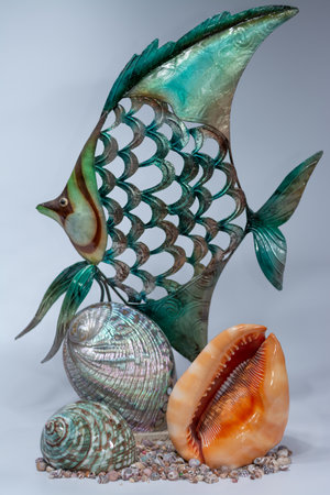 A vertical shot of a fish figurine with different seashells under it on a white surface and backgroundの写真素材