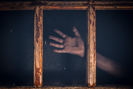 A creepy image of a hand on a glass window at nightの写真素材