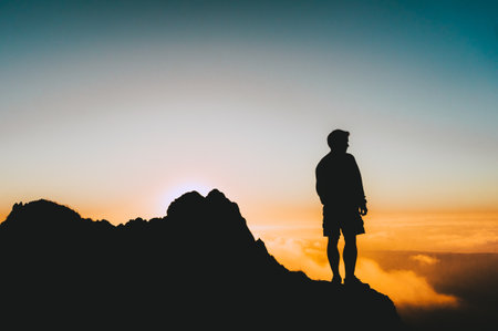A silhouette shot of a man standing on a cliff looking at the sunsetの写真素材
