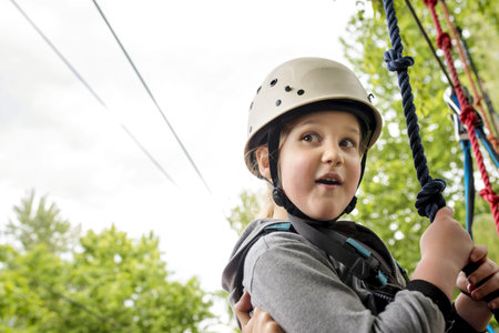 A closeup shot of a caucasian female child wearing a white helmet and adventure park gear hanging onto a ropeの写真素材