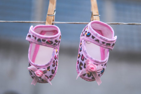 A pair of cute, pink-colored baby shoes with brown dots hanging from the wire with wooden clothespinsの写真素材