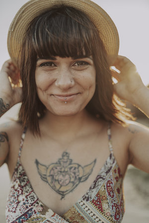 A closeup of a young caucasian female with tattoos wearing a dress and straw hat