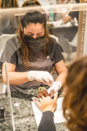 A shallow focus vertical shot of a Hispanic female nail artist wearing a mask painting a client's nailsの写真素材