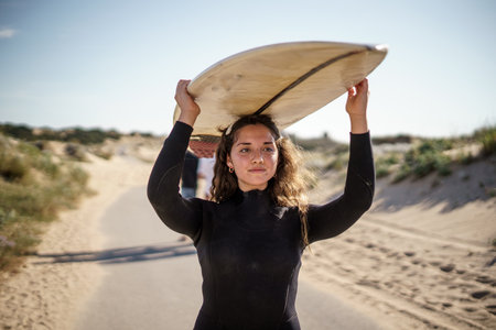 A shallow focus shot of a European female holding a surfboard and walking to the beach