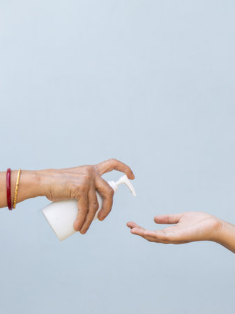 A closeup shot of a person pouring liquid soap into the hand of another person - importance of washing hands during the COVID-19 pandemicの写真素材
