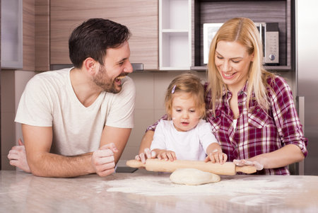 A happy couple with their little daughter baking in the kitchenの写真素材