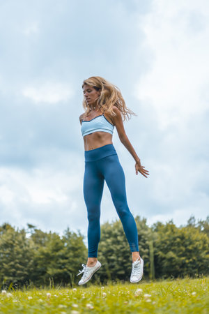 A vertical shot of a female model stretching her body by jumping on background of a garden