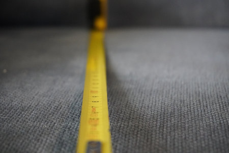 A closeup shot of a yellow measuring tape on the gray carpet