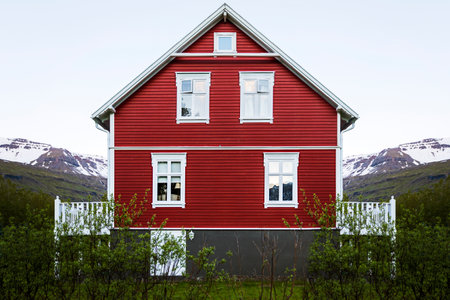 The beautiful facade of a wooden red house with white windows and balconies on a green fieldの写真素材