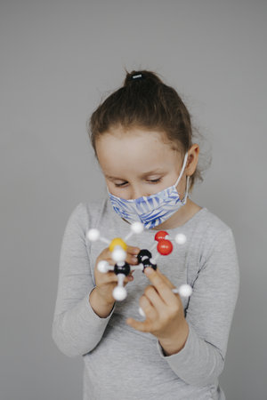 A Caucasian female child with a protective medical face mask playing with Coronavirus cell model - Prevention of the epidemic of Covid-19の写真素材