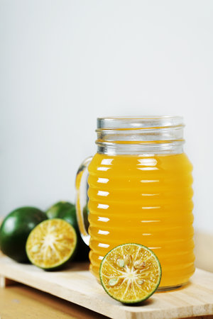 A vertical shot of calamansi lime  juice in a glass with fresh calamnsi limes on a wooden board