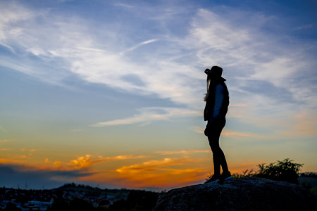 A European female with cowboy hat standing on a rock and watching the sunsetの写真素材