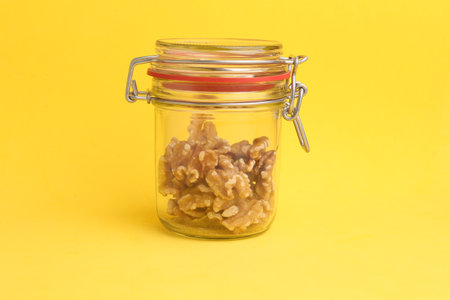 A closeup of walnuts in a glass jar with a lid on a yellow backgroundの写真素材