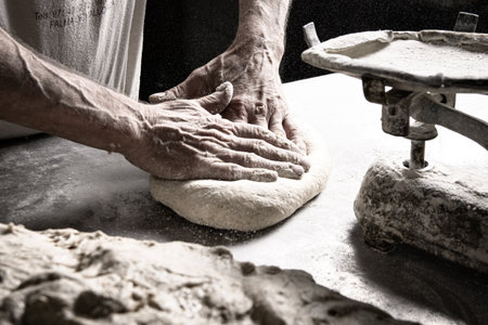 A closeup shot of a chef massaging a piece of dough on a table covered in flour next to a scale