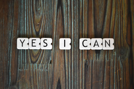 A closeup shot of square-shaped letters of "yes I can" on a textured wooden tableの写真素材