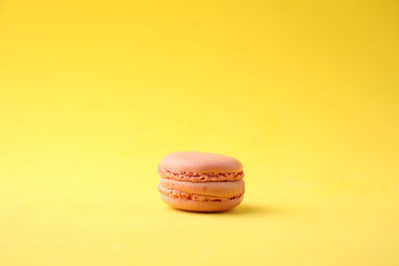 A closeup shot of a pink macaroon on a yellow backgroundの写真素材