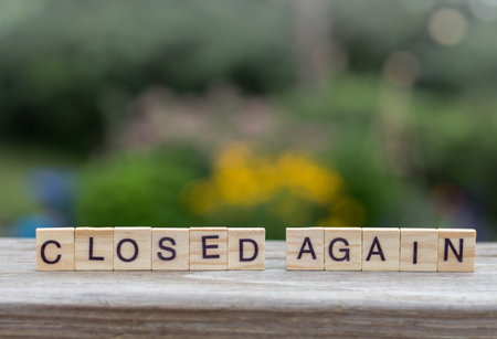 A closeup of a CLOSED AGAIN text written with wooden letter cubes with a blurry background