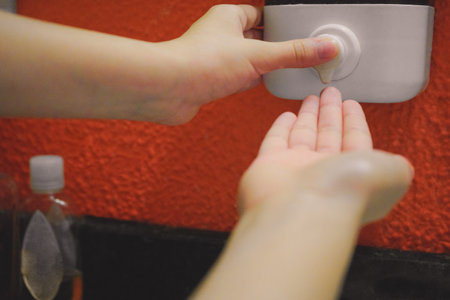 A closeup shot of a person's hands using wall mounted liquid dispenser - the concept of hygiene