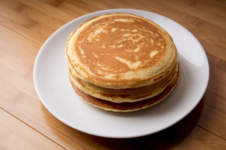 A high angle shot of freshly baked pancakes on a white plate on a wooden tableの写真素材