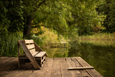 A wooden bench on the deck on the lake surrounded by greensの写真素材