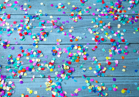 A top view of colorful round confetti on a light blue wooden background