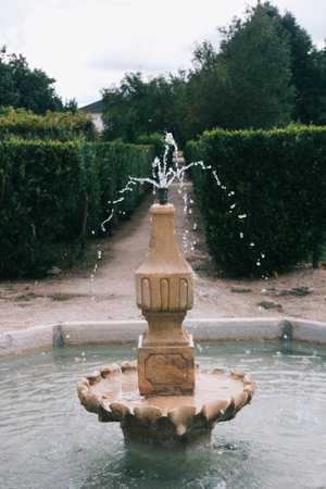A vertical shot of a water fountain in the center of a green gardenの写真素材