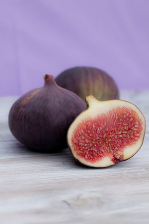 A vertical shot of fresh figs cut in half on a wooden surface and purple backgroundの写真素材