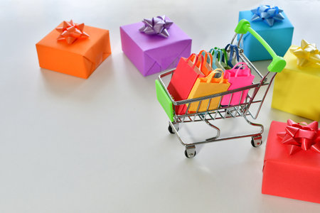 A closeup shot of gift boxes and a shopping cart filled with colorful paper bagsの写真素材