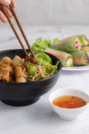 A vertical shot of a person eating Vietnamese grilled pork on noodles using chopsticks, with fish...
