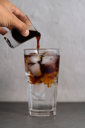 A vertical shot of a person making Vietnamese iced coffee by pouring a glass of espresso into a glass of iced waterの写真素材