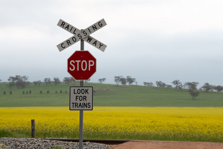 A sign that says 'Crossing Railway Stop Look for trains' posted on the side of the tracks with a beautiful meadow on the backgroundの写真素材