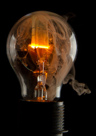 A vertical shot of a burning light bulb with smoke coming out of it isolated on a black backgroundの写真素材