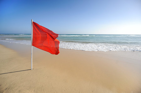 A warning sign of a red flag at a beautiful beach with a blue sky and a turquoise seaの写真素材