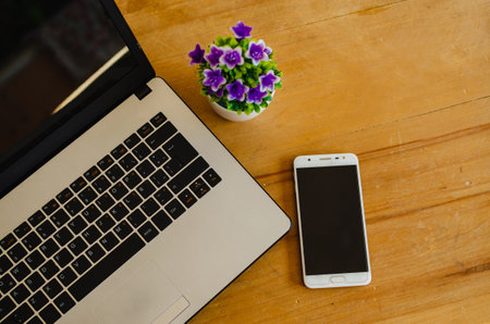 A high angle closeup shot of a laptop and a smartphone next to on a pot of flowers wooden tableの写真素材