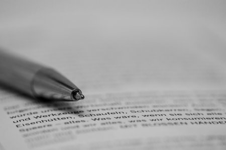 A greyscale closeup shot of a pen on a printed paper with writing in Germanの写真素材
