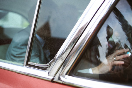 A groom and a bride sitting in a red vintage car