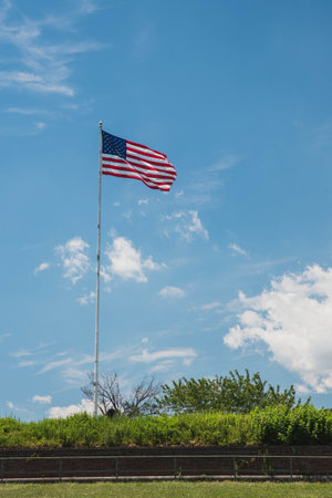 A vertical shot of an American flag waving on a pole with a blue sky background