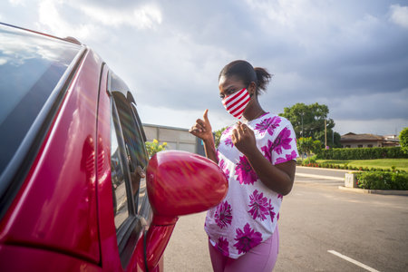A young black female wearing a medical mask getting ready to go into a car