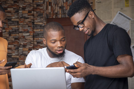 A group of young African males discussing a project while using their laptop and phones