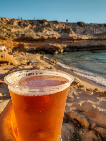 A vertical shot of a cup of beer with a blurry coastal cliff in the backgroundの写真素材