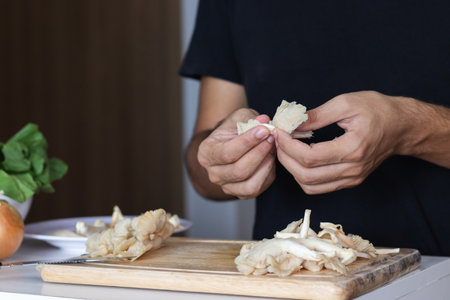 A closeup shot of a cutting board and a young man cutting  oyster mushroomsの写真素材