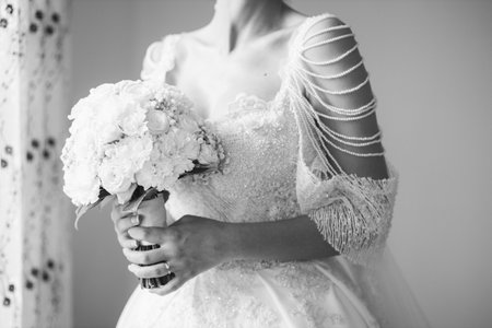 A grayscale shot of an elegant bride holding a beautiful bouquet of flowersの写真素材