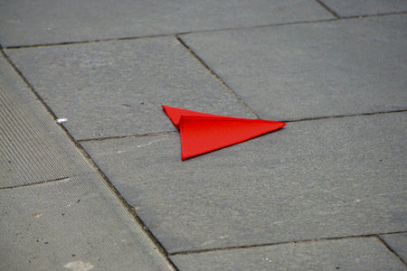 A bright red paper plane laying on a gray cement floorの写真素材