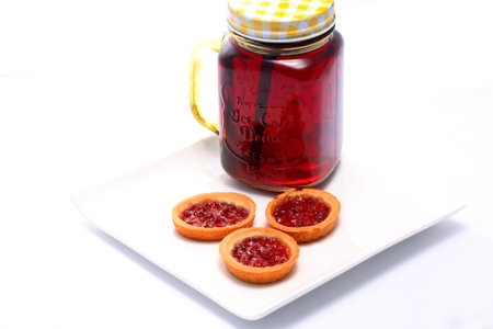 A closeup shot of mini tartlets with jam and raspberry jam in a jar on a white plate