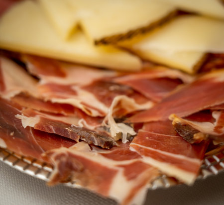 A closeup of Jamon serrano slices and cheese pon a plate on the tableの写真素材