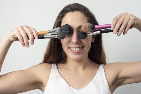 A closeup shot of a cheerful young lady closing her eyes with different makeup brushes