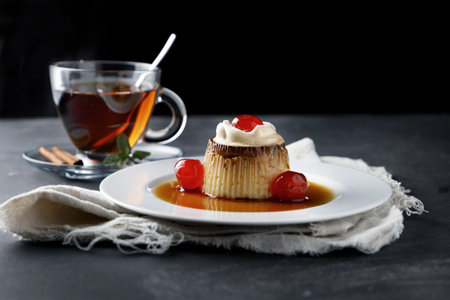 A selective focus shot of delicious flan with sour cherries and tea with cinnamon