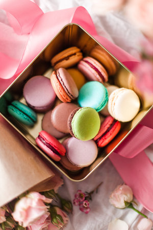 A vertical top view of a box of colorful macarons decorated with pastel pink colorsの写真素材