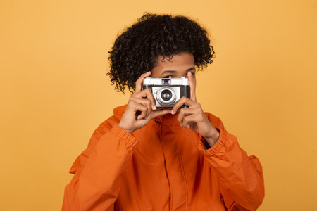 A young African American man in an orange raincoat with a vintage retro photographic cameraの写真素材
