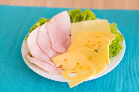 A white plate of cheese, ham and vegetables on a blue surfaceの写真素材